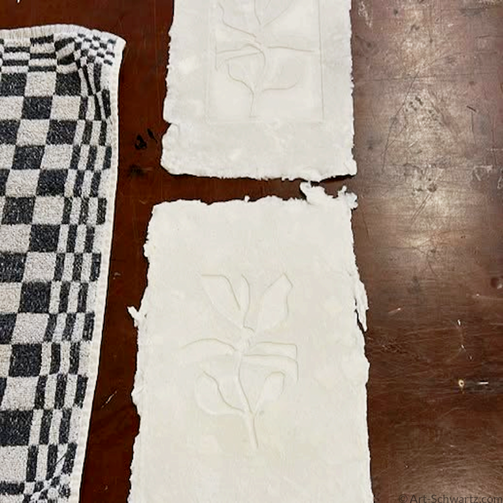 Twee vellen handgeschept papier met blinddruk van een blad, op een theedoek