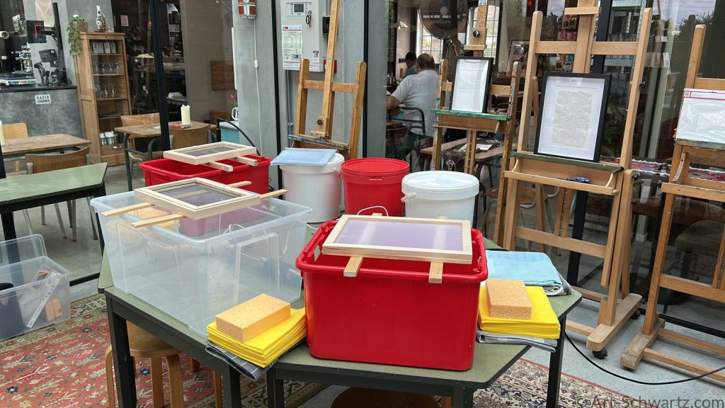 Werktafel met schepramen, emmers pulp en drooprekken voor de workshop handgeschept papier maken